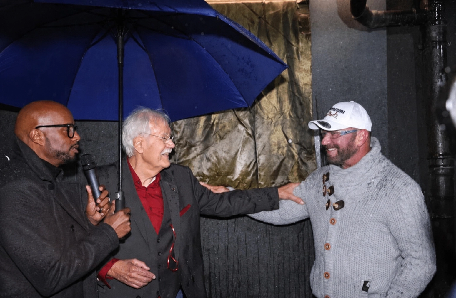 Carlo von Tiedemann lacht im Gespräch mit dem Handwerker unter dem Regenschirm