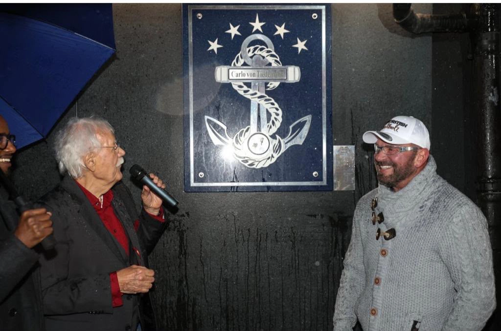 Carlo von Tiedemann mit Mikrofon neben seiner Ankertafel